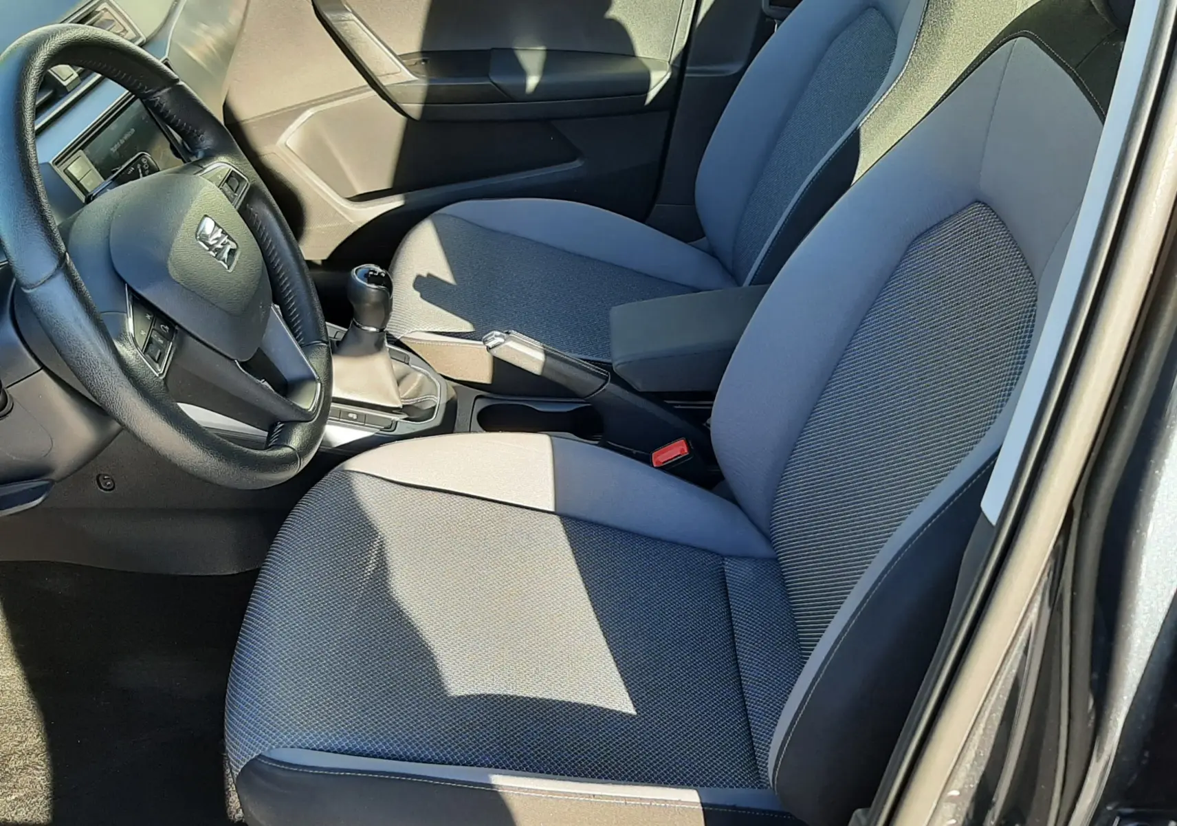 Vue intérieure côté conducteur de la SEAT Arona 2019, sièges tissu gris et volant multifonction noir.