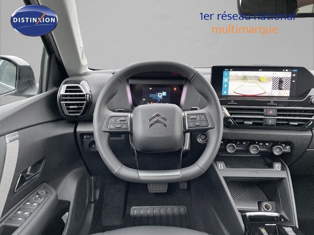 Vue intérieure frontale du poste de conduite de la Citroën C4 gris platinium, avec volant multifonction et écran tactile affichant la caméra de recul.