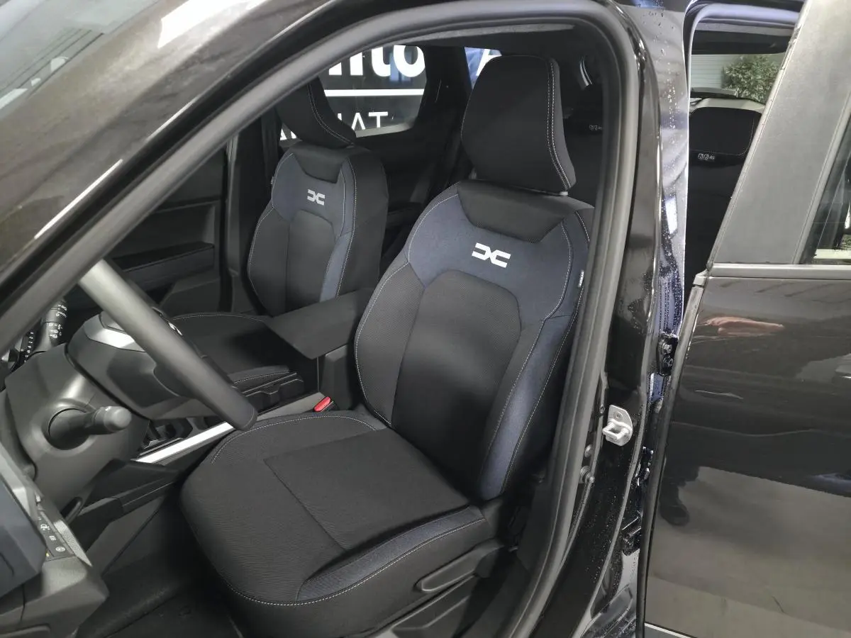 Vue intérieure côté conducteur du Dacia Duster 1.6 Hybrid 2025 noir, sièges tissu Denim avec logo DC brodé.