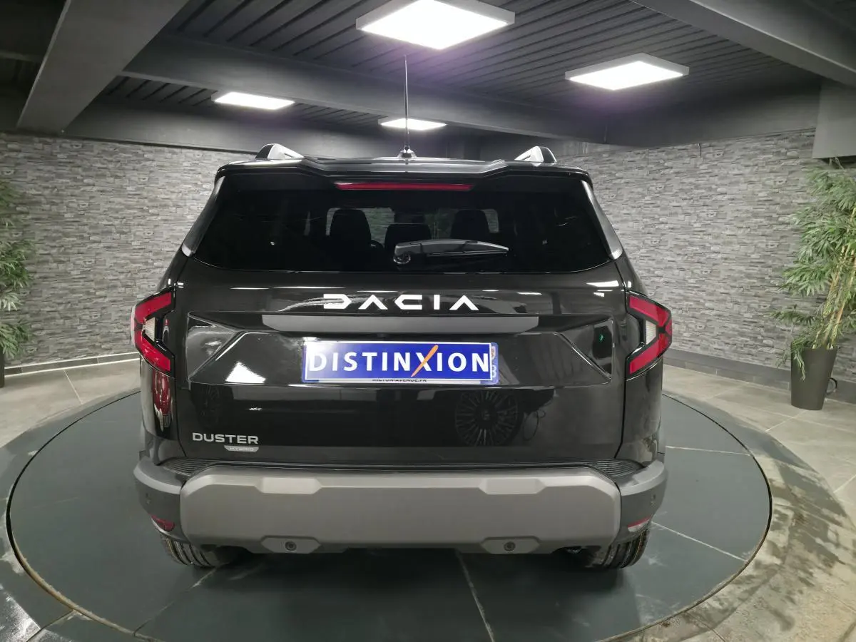 Vue arrière d'un Dacia Duster 1.6 Hybrid noir nacré avec logo DACIA lumineux et bouclier arrière gris dans un showroom.