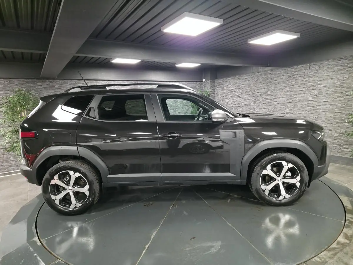 Profil droit du Dacia Duster 1.6 Hybrid 140 Journey noir nacré avec jantes alliage diamantées en intérieur showroom.