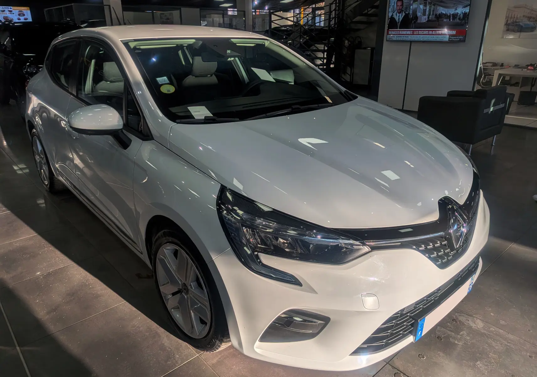 Renault Clio V Blue dCi 85 Business blanc glacier vue 3/4 avant droit en intérieur showroom.