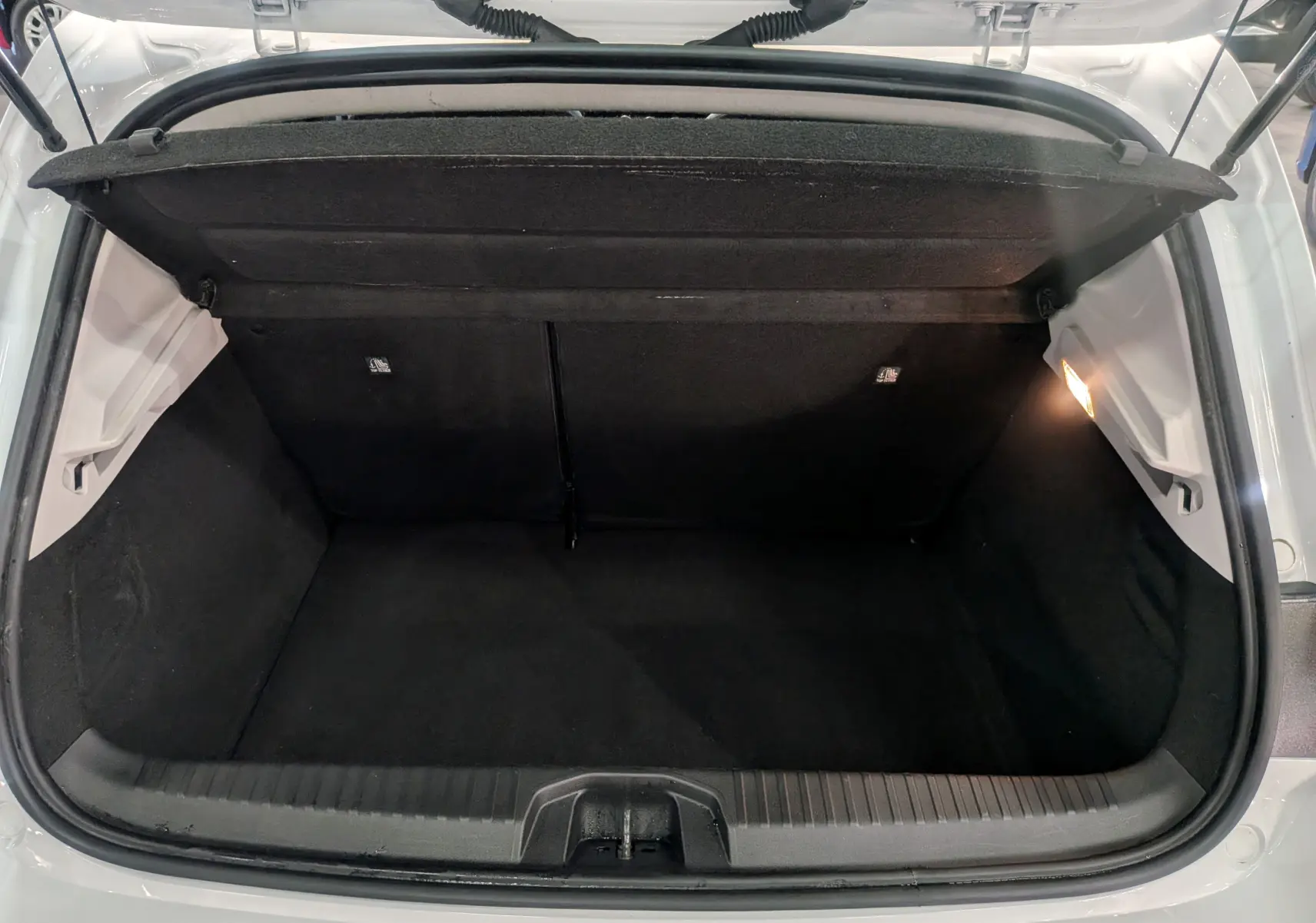 Vue plongeante sur le coffre ouvert d'une Renault Clio V Blanc Glacier, montrant un espace de rangement propre et éclairé.
