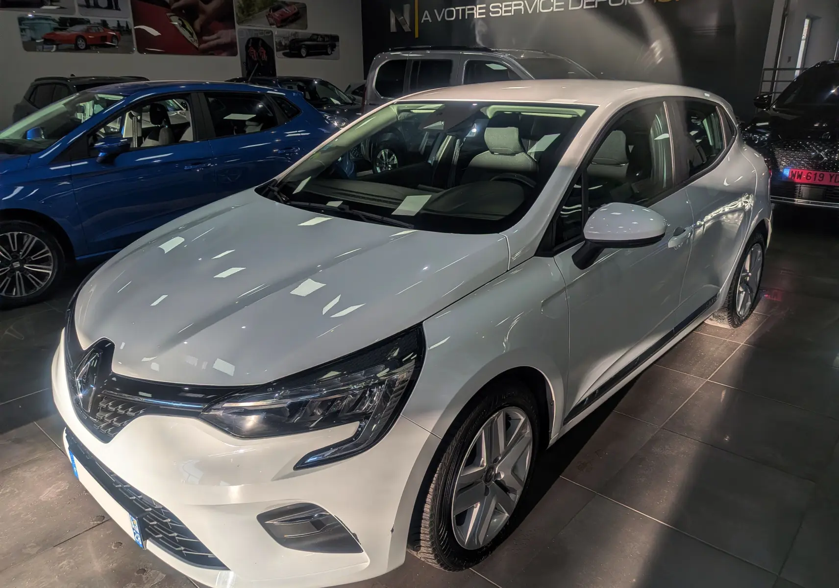 Renault Clio V Blue dCi 85 Business blanc glacier vue 3/4 avant droit en intérieur showroom.
