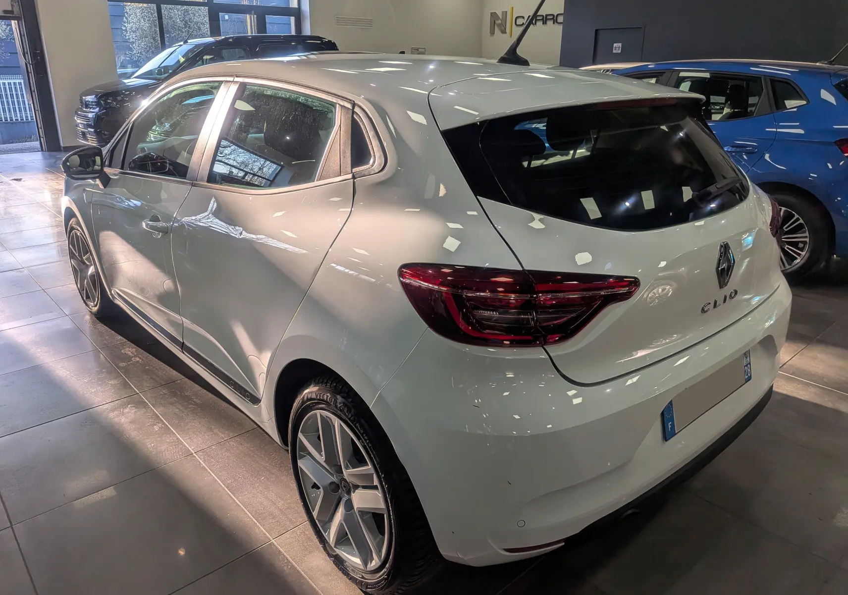 Vue 3/4 arrière droite d'une Renault Clio V Blanc Glacier en intérieur, avec feux arrière LED et jantes alliage distinctives.