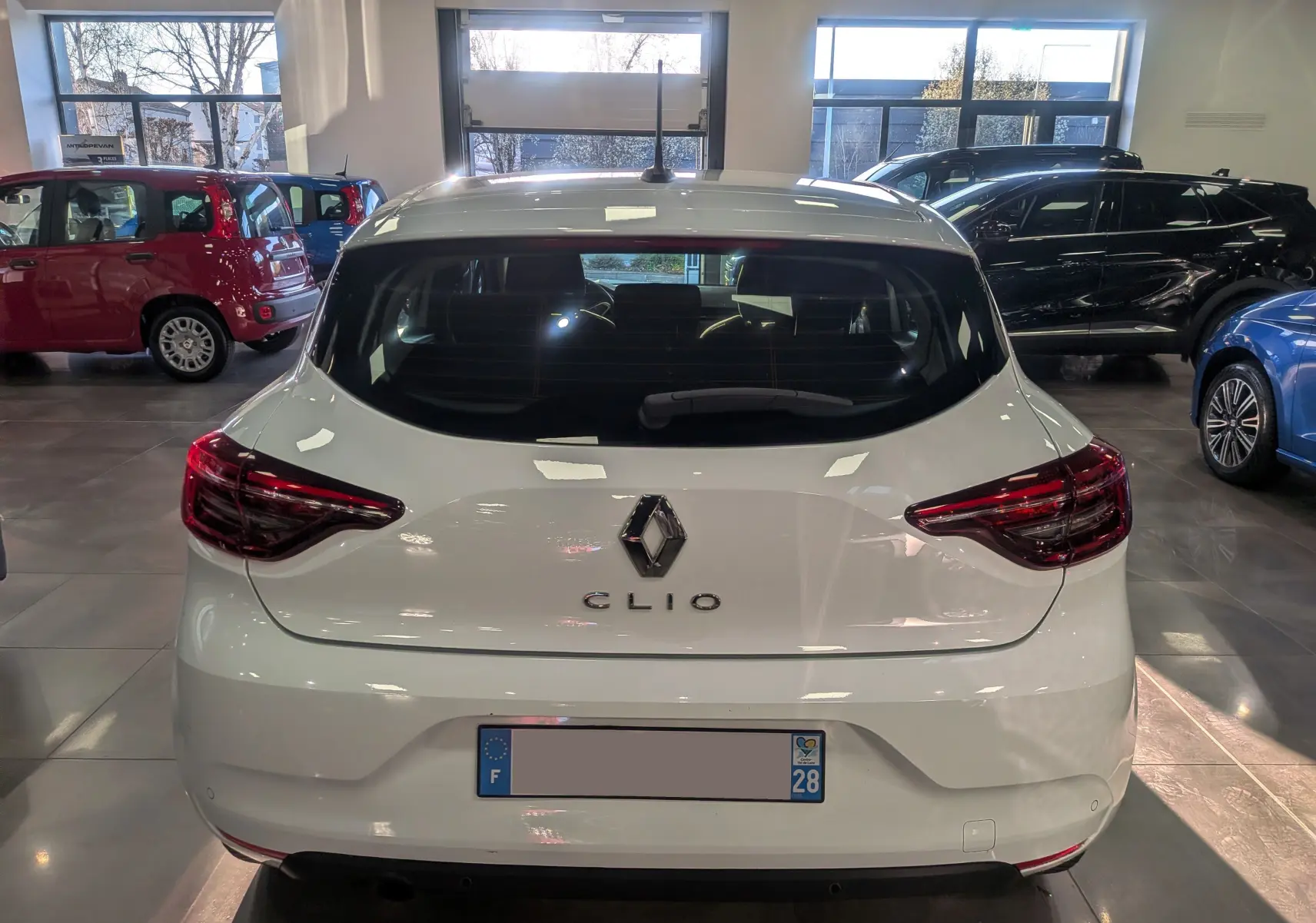 Vue arrière d'une Renault Clio V Blanc Glacier 2021 en showroom, avec feux arrière LED et logo central visible.