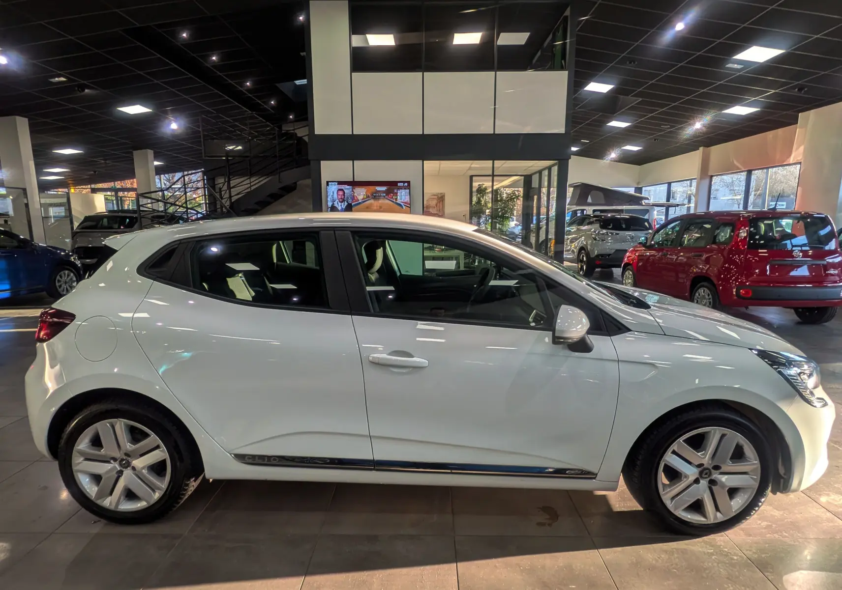 Profil côté gauche d'une Renault Clio V Blanc Glacier 2021 en showroom, avec jantes alliage et poignées de porte ton carrosserie.