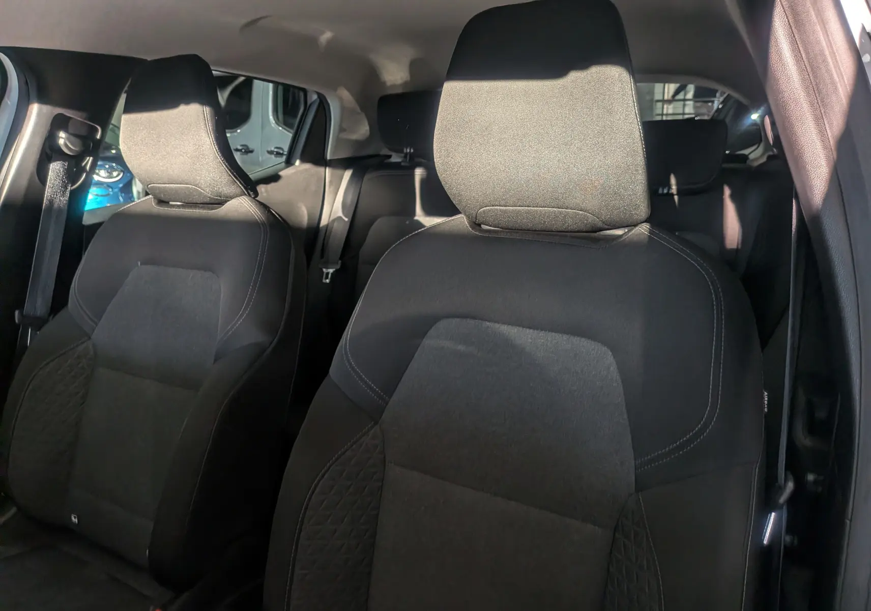 Vue intérieure sur les sièges avant en tissu noir de la Renault Clio V Business, avec lumière naturelle sur l'habitacle.