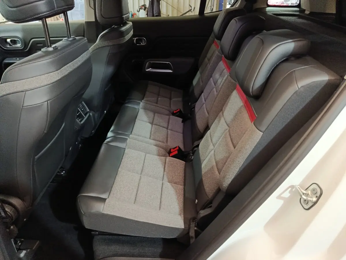 Vue intérieure côté droit sur les sièges arrière gris et noirs du Citroën C5 Aircross Hybrid blanc, avec appuie-têtes et ceinture rouge.
