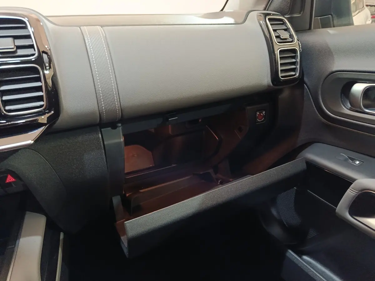 Vue intérieure côté passager du tableau de bord gris et noir avec boîte à gants ouverte du Citroën C5 Aircross Hybrid blanc.