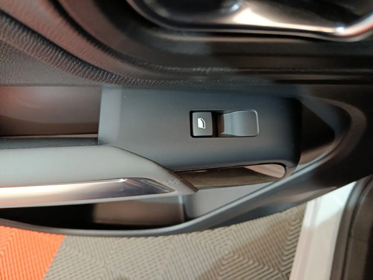 Gros plan sur le bouton de commande de vitre côté conducteur dans l’intérieur noir du Citroën C5 Aircross blanc hybride.
