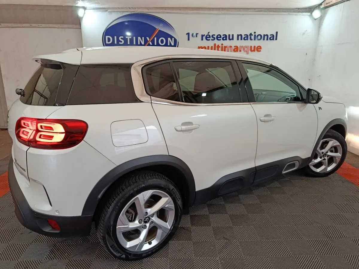 Vue 3/4 arrière droite d'un Citroën C5 Aircross Hybrid blanc avec feux arrière LED allumés en intérieur showroom.