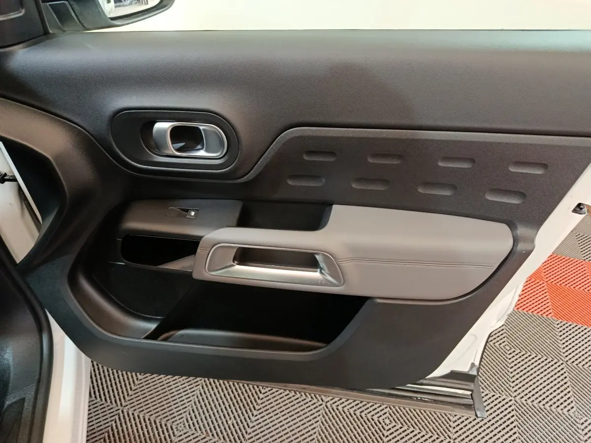 Intérieur côté gauche de la porte avant blanche du Citroën C5 Aircross Hybrid avec poignée grise et commandes vitrées.