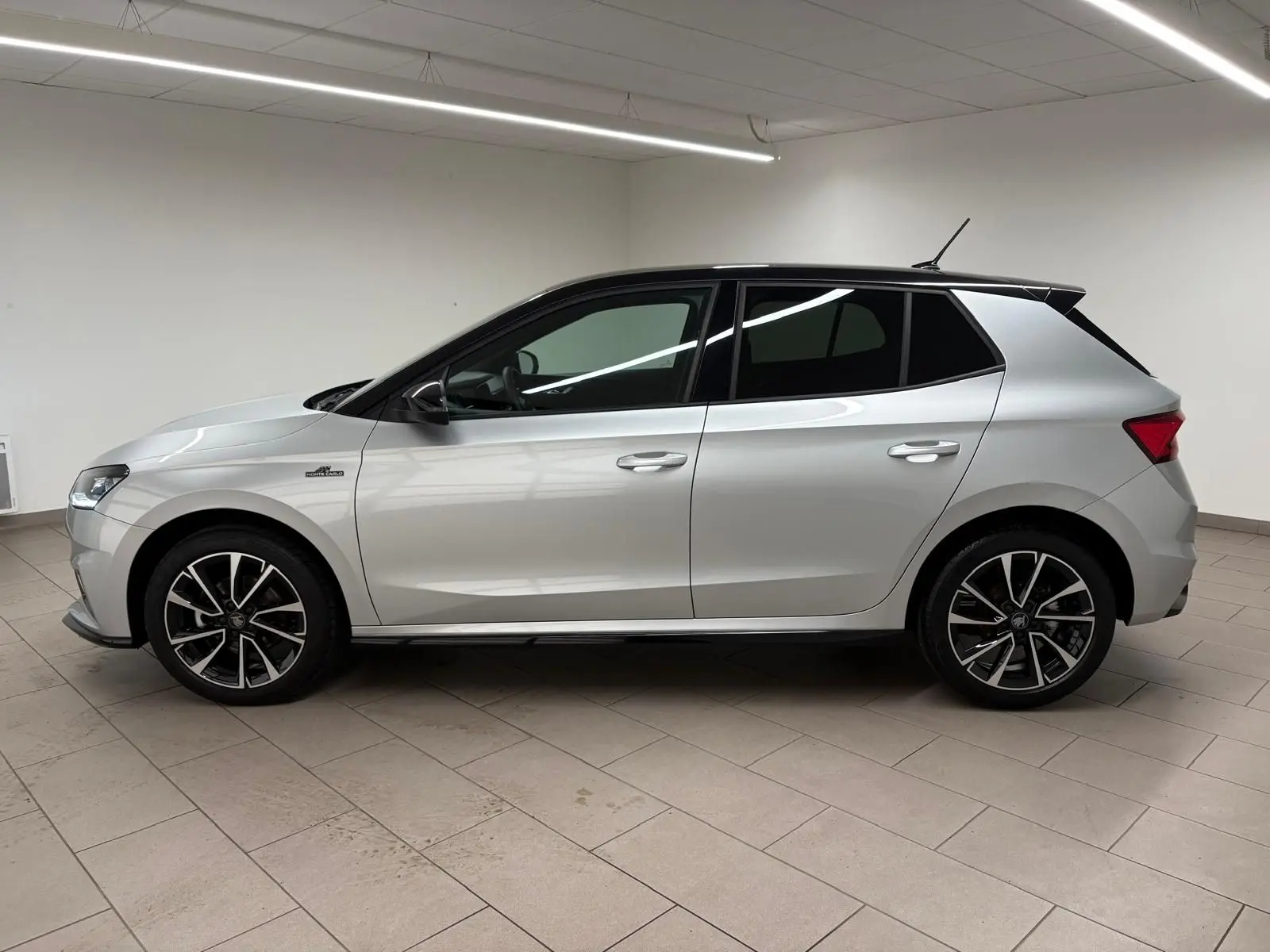 Vue de profil côté gauche d'une Skoda Fabia 2025 gris argent avec toit noir et jantes alliage noires.