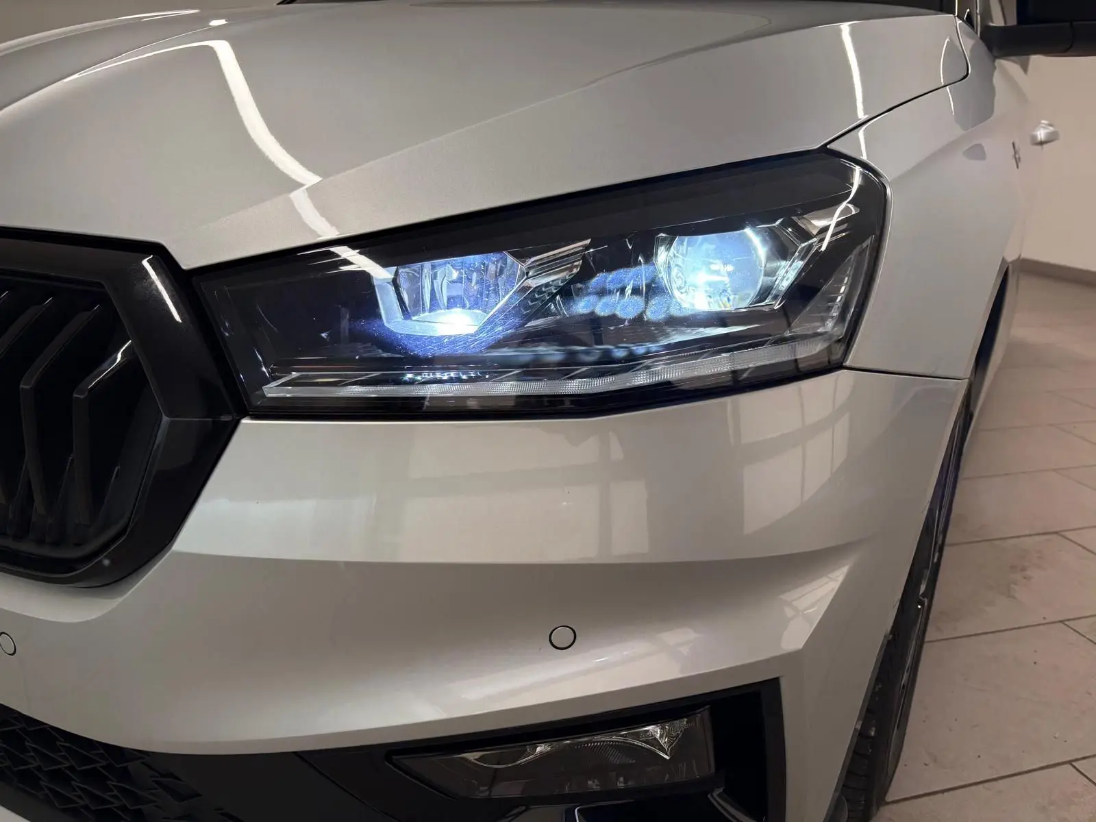 Gros plan sur le phare avant droit allumé d'une Skoda Fabia 2025 gris argent avec toit noir, version Monte Carlo.