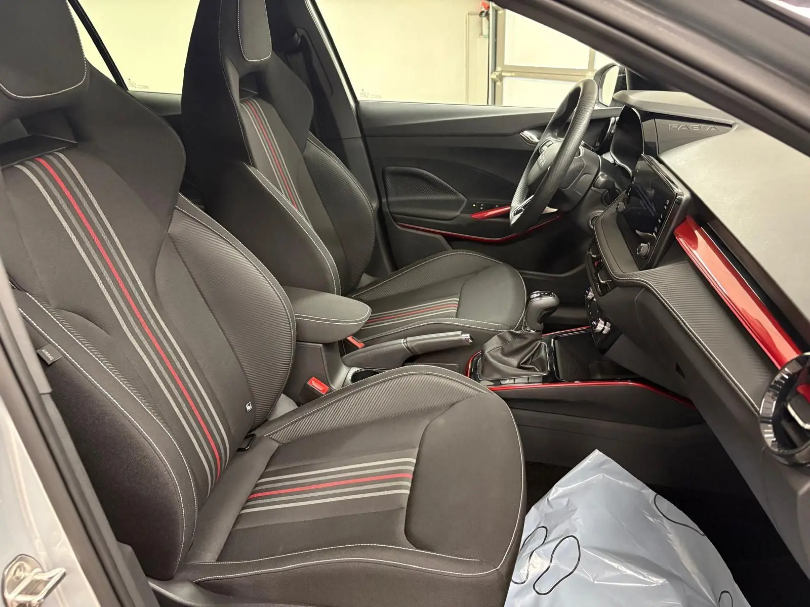 Vue intérieure côté conducteur de la Skoda Fabia 2025, sièges noirs avec bandes rouges et tableau de bord avec inserts rouges.