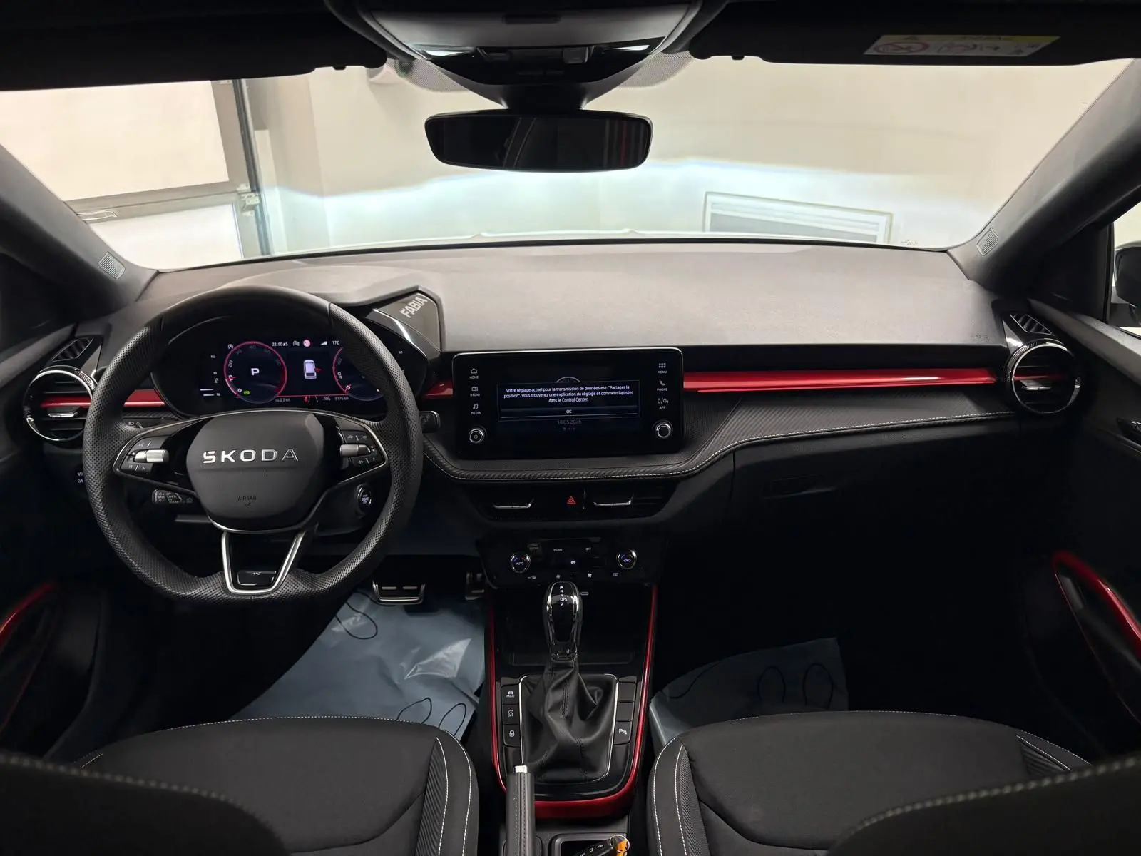 Vue intérieure avant de la Skoda Fabia 2025, tableau de bord noir avec accents rouges et volant multifonction.