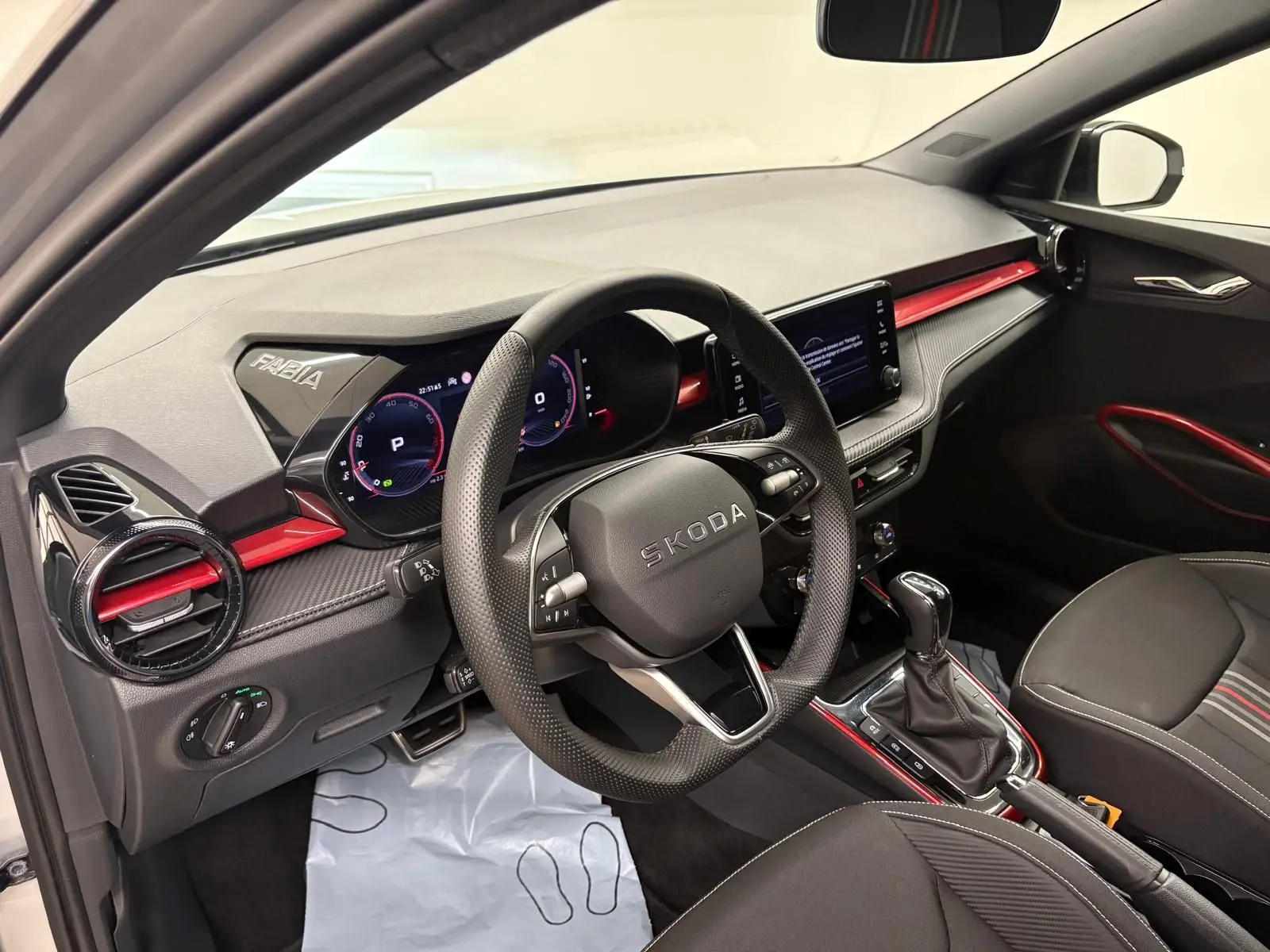 Vue intérieure côté conducteur de la Skoda Fabia 2025, tableau de bord noir avec touches rouges et volant multifonction.