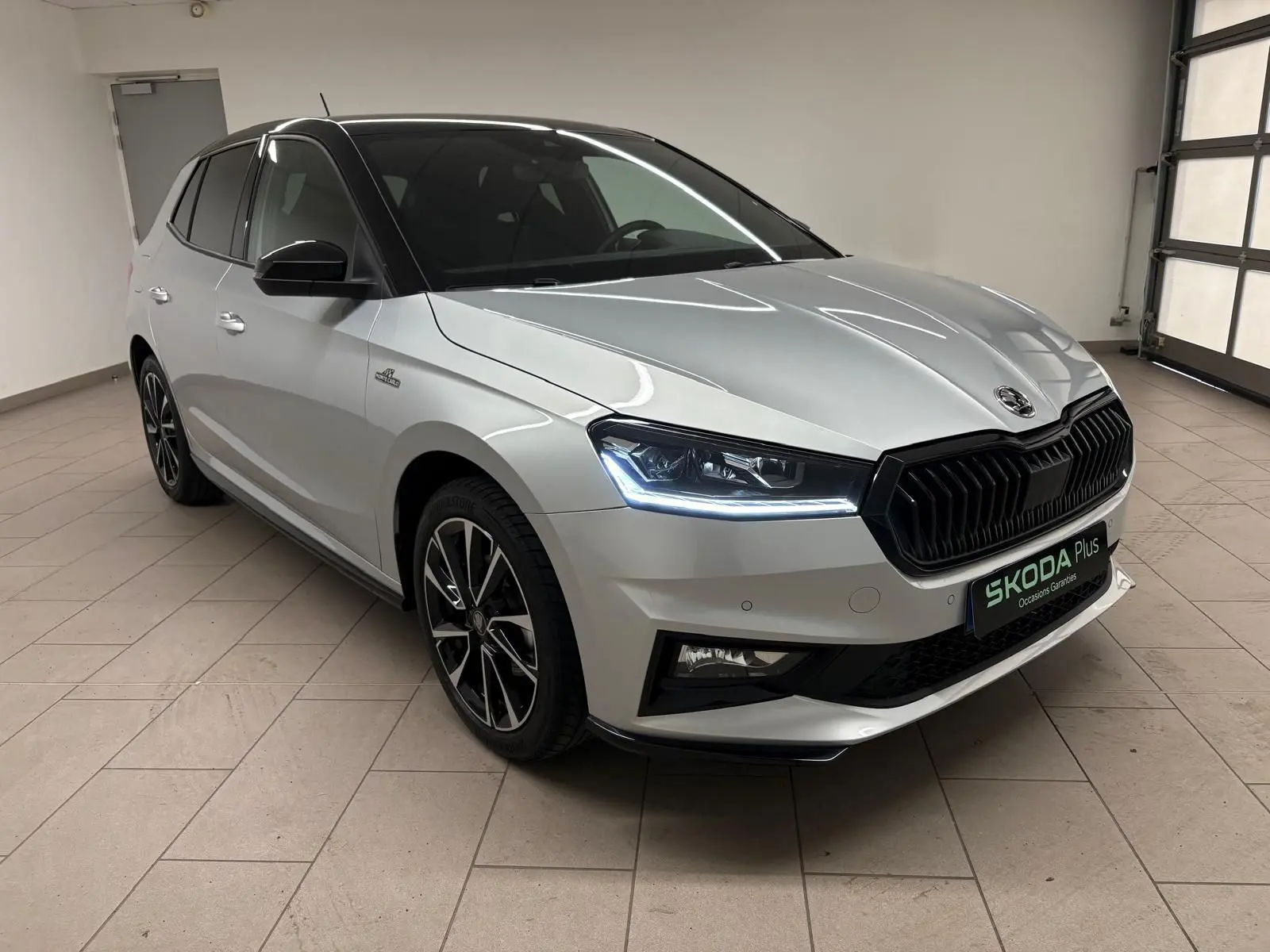 Vue 3/4 avant droite d'une Skoda Fabia 2025 gris argent avec toit noir et calandre noire distinctive.
