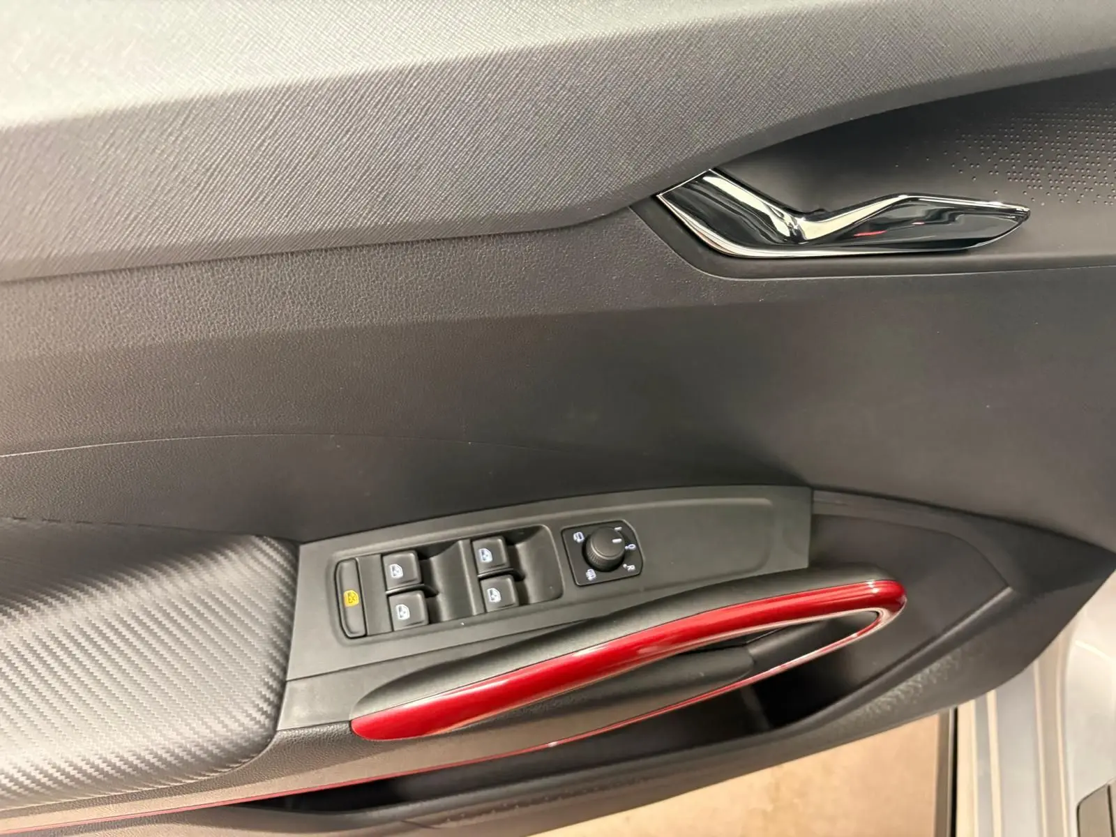 Vue intérieure du panneau de porte côté conducteur de la Skoda Fabia 2025, avec poignée rouge et commandes de vitres noires.