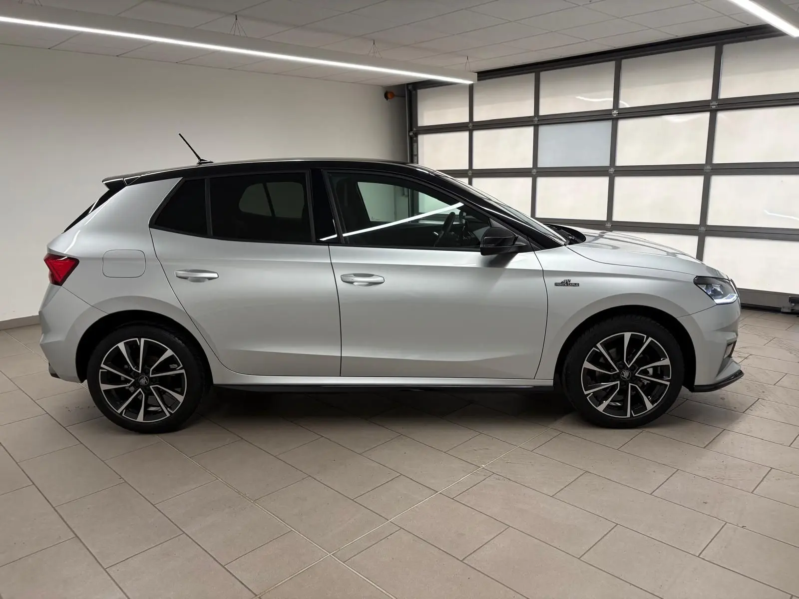 Vue de profil côté gauche de la Skoda Fabia 1.0 TSI Monte Carlo gris argent avec toit noir et jantes noires.