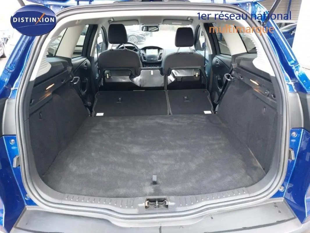 Vue arrière du coffre ouvert d'une Ford Focus SW bleu foncé, sièges arrière rabattus pour un grand espace de chargement.