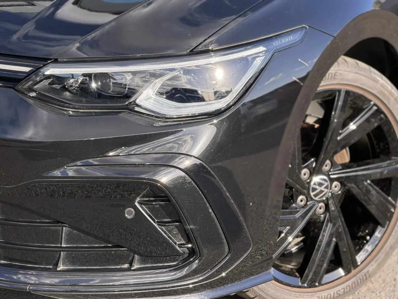 Gros plan sur l'avant droit noir brillant d'une Volkswagen Golf 8 R-Line avec phare IQ.Light et jante alliage noir.