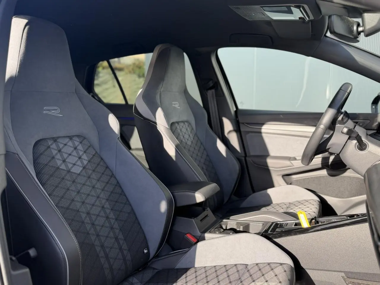 Vue intérieure côté gauche de la Volkswagen Golf 8 R-Line 2024 avec sièges sport gris à motifs et volant cuir noir.