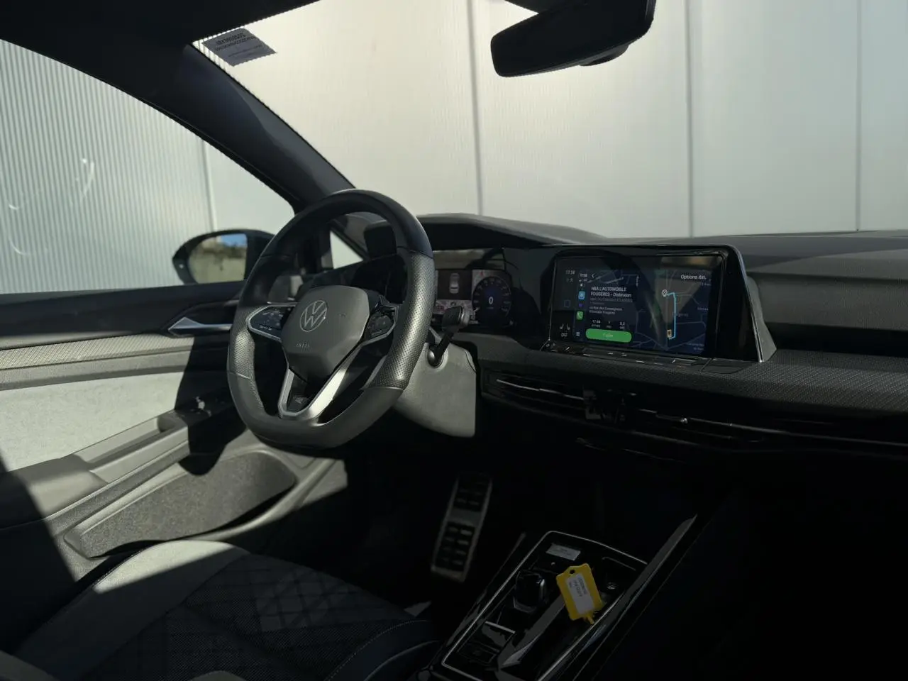 Vue intérieure côté conducteur de la Volkswagen Golf 8 noire avec volant sport multifonction et écran tactile central.