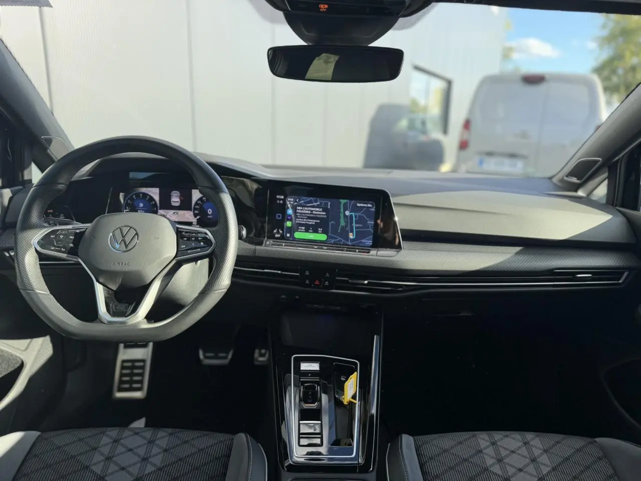 Vue intérieure avant de la Volkswagen Golf 8 noire, avec tableau de bord numérique et écran tactile central.