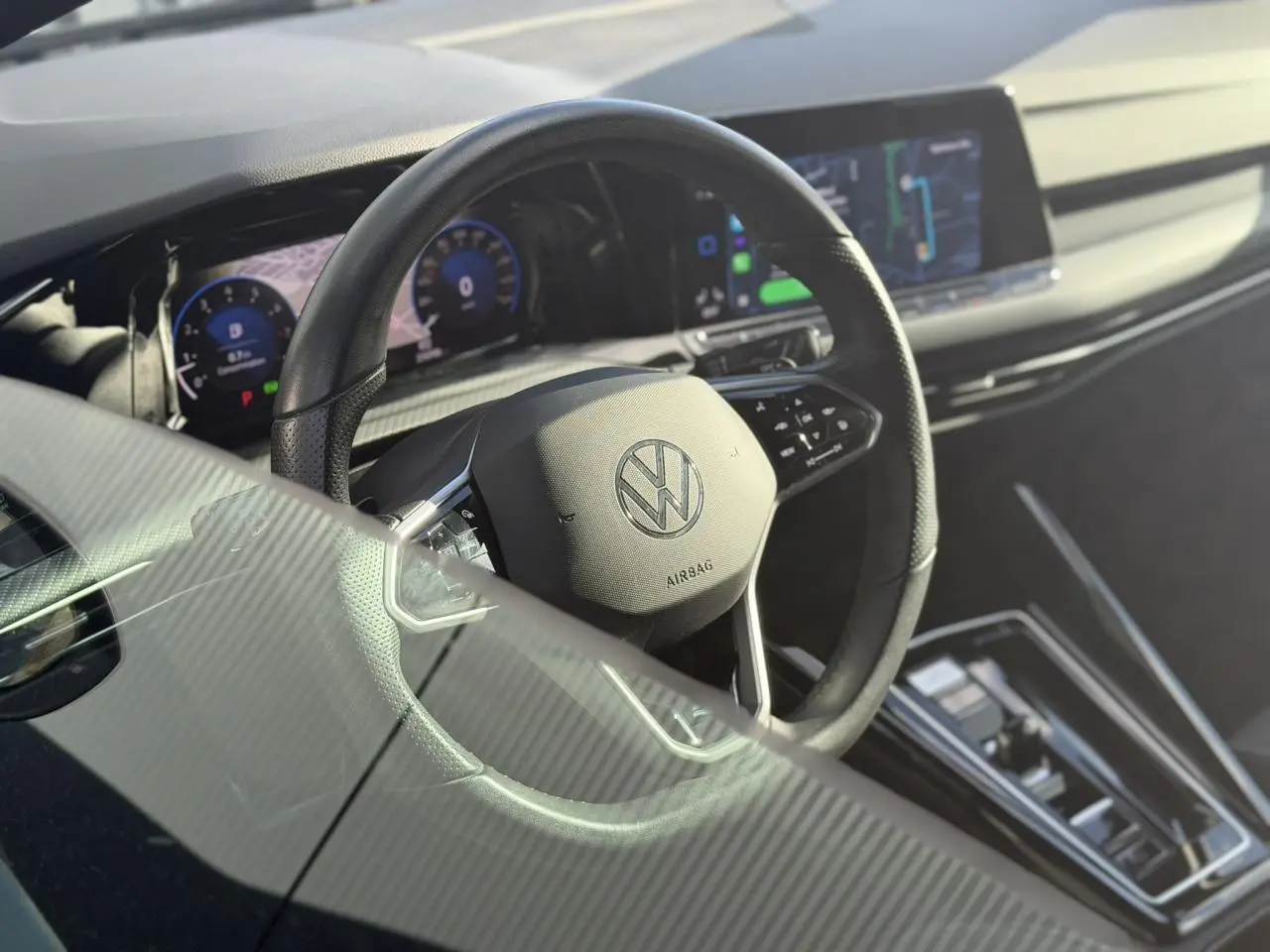 Vue intérieure centrée sur le volant cuir multifonction d'une Volkswagen Golf 8 noire avec tableau de bord numérique et écran tactile.
