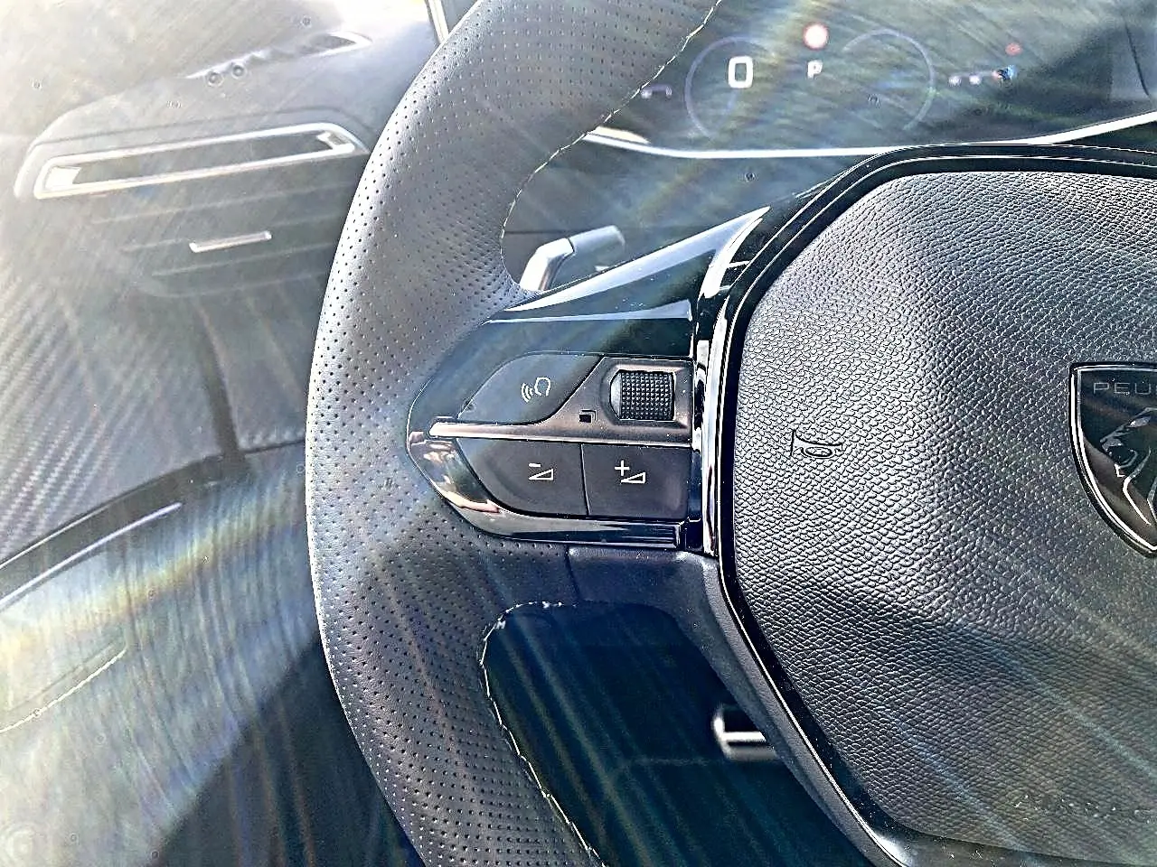 Gros plan sur le volant cuir perforé noir de la Peugeot 2008 1.2 hybrid 145 GT avec commandes intégrées.