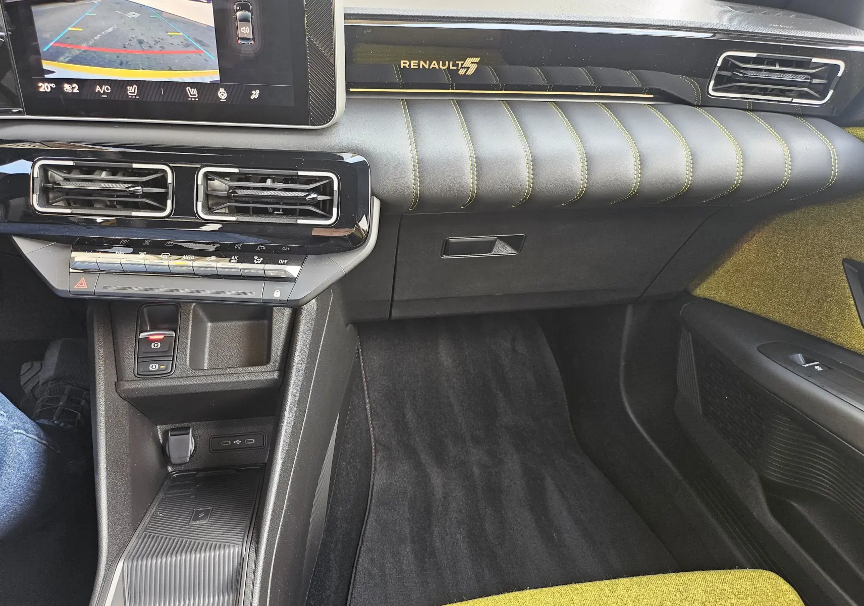 Vue intérieure côté passager de la Renault R5 Iconic 2025, tableau de bord noir avec surpiqûres jaunes et logo Renault éclairé.