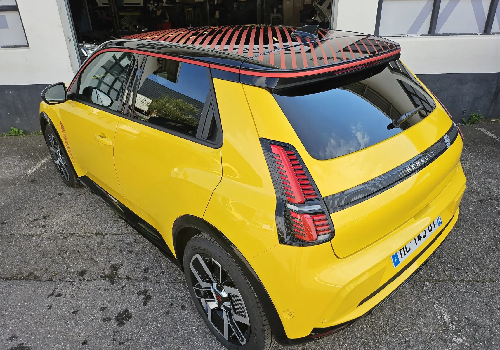 Vue 3/4 arrière droite d'une Renault R5 électrique 2025 jaune pop avec toit noir à rayures rouges et feux arrière LED.