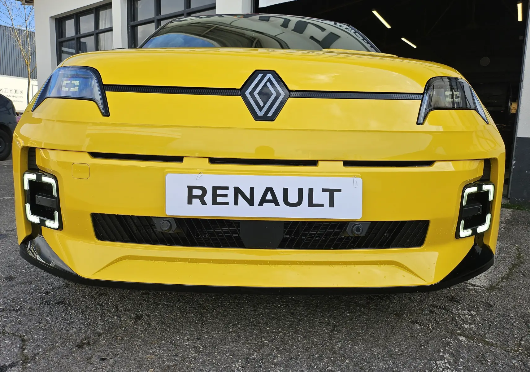 Vue frontale rapprochée de la Renault R5 Iconic jaune pop avec phares LED carrés et toit noir visible.