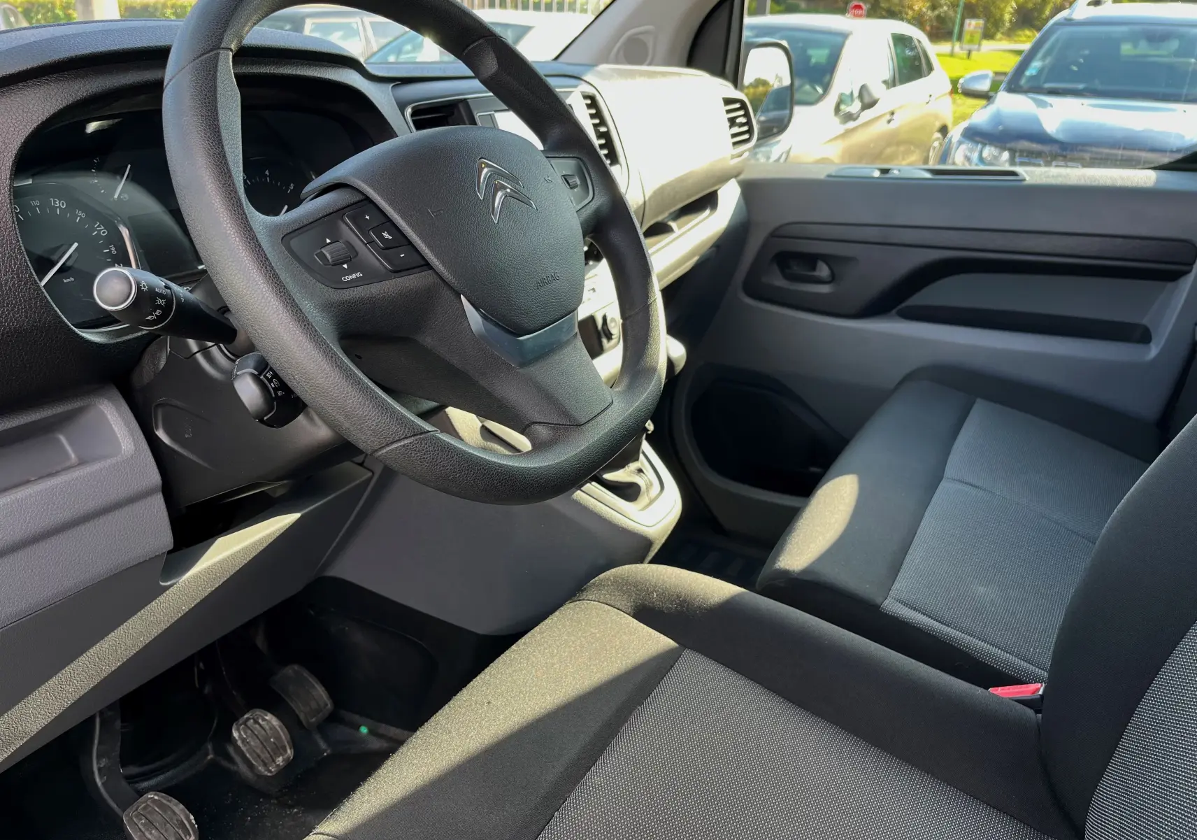 Vue intérieure côté conducteur du Citroën Jumpy 2022, volant noir, sièges gris et tableau de bord clair.