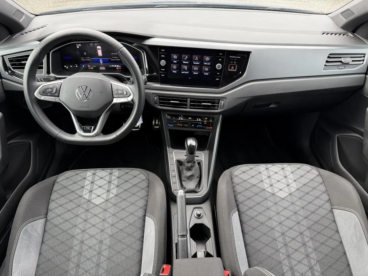 Intérieur avant de la Volkswagen Polo 2025, volant cuir multifonction, écran tactile 8 pouces et sièges tissu gris à motifs.