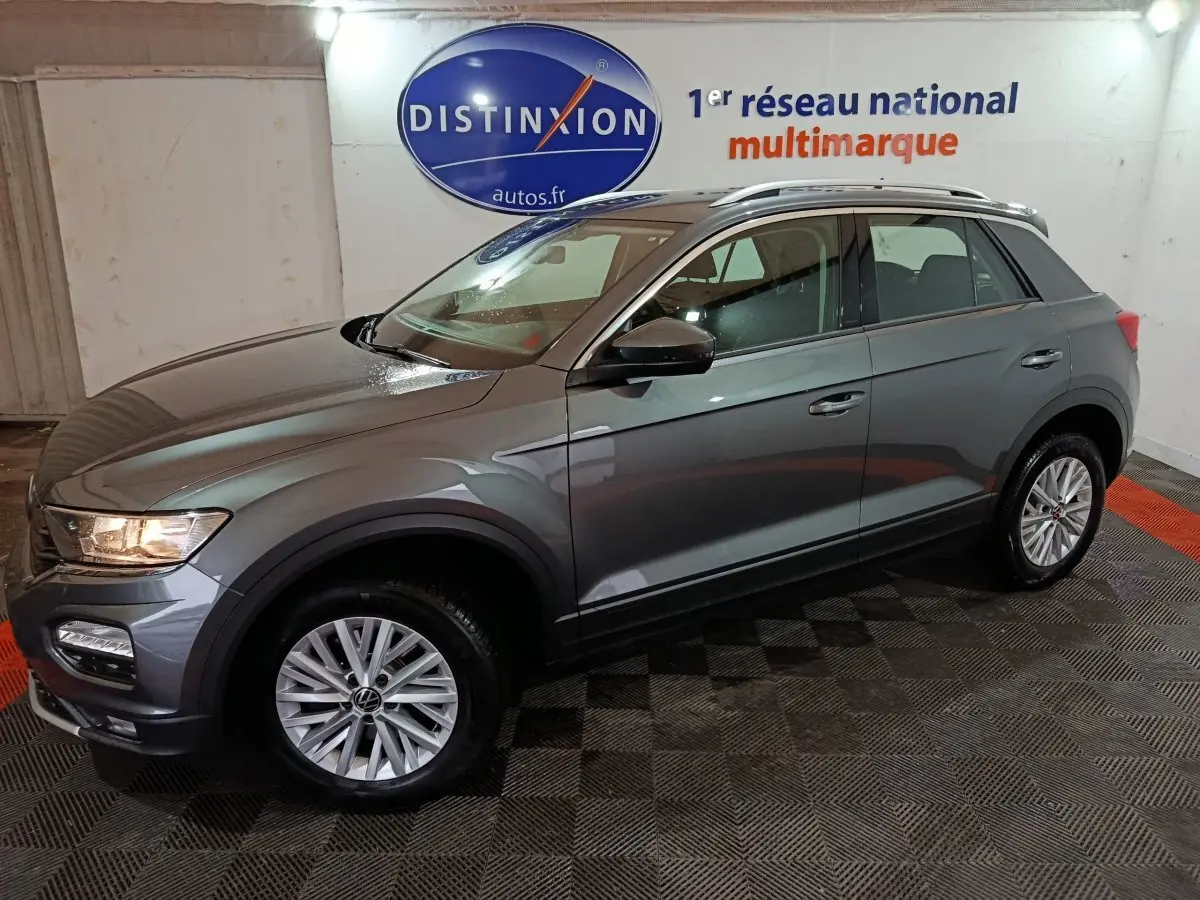 Volkswagen T-Roc gris foncé vue de profil droit en intérieur, avec jantes alliage et barres de toit chromées.