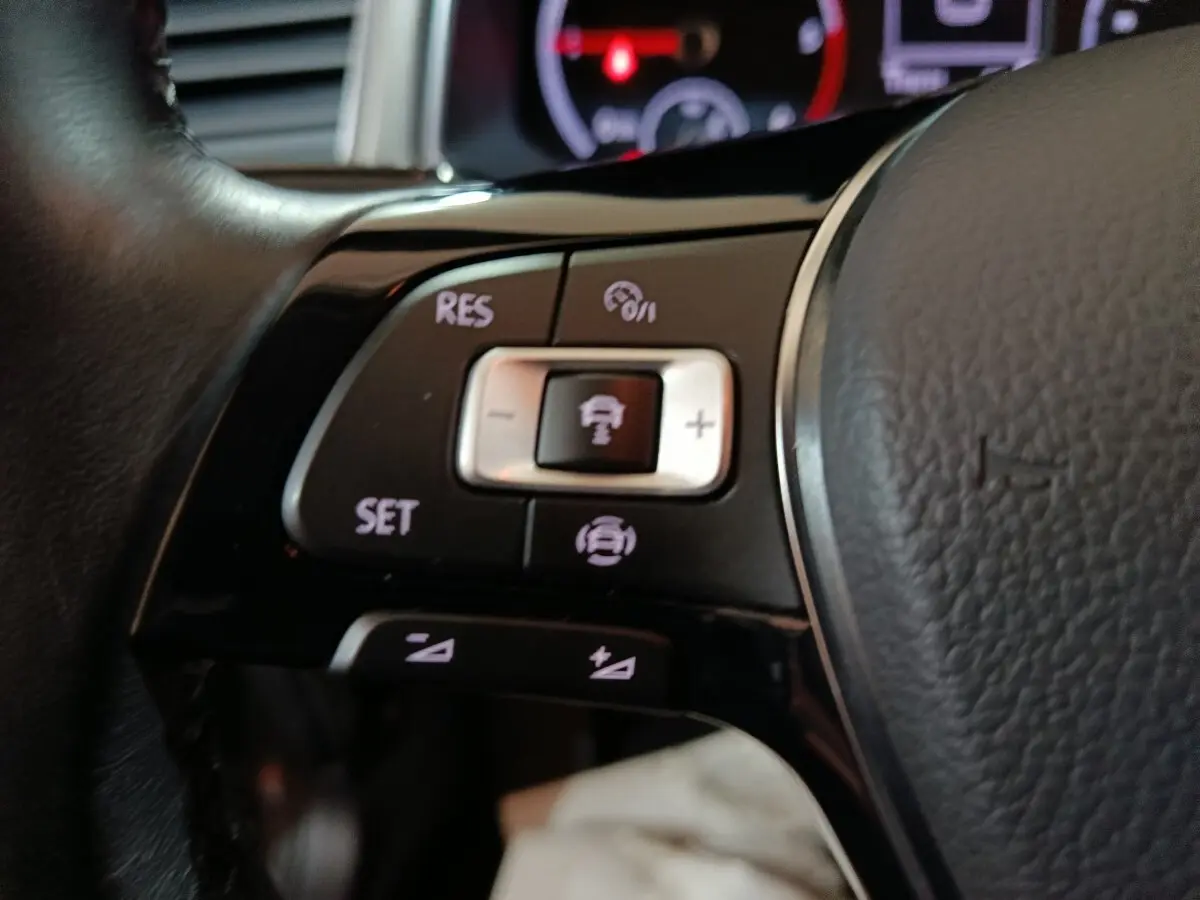 Gros plan sur les commandes de régulateur de vitesse au volant cuir noir du Volkswagen T-Roc gris foncé.