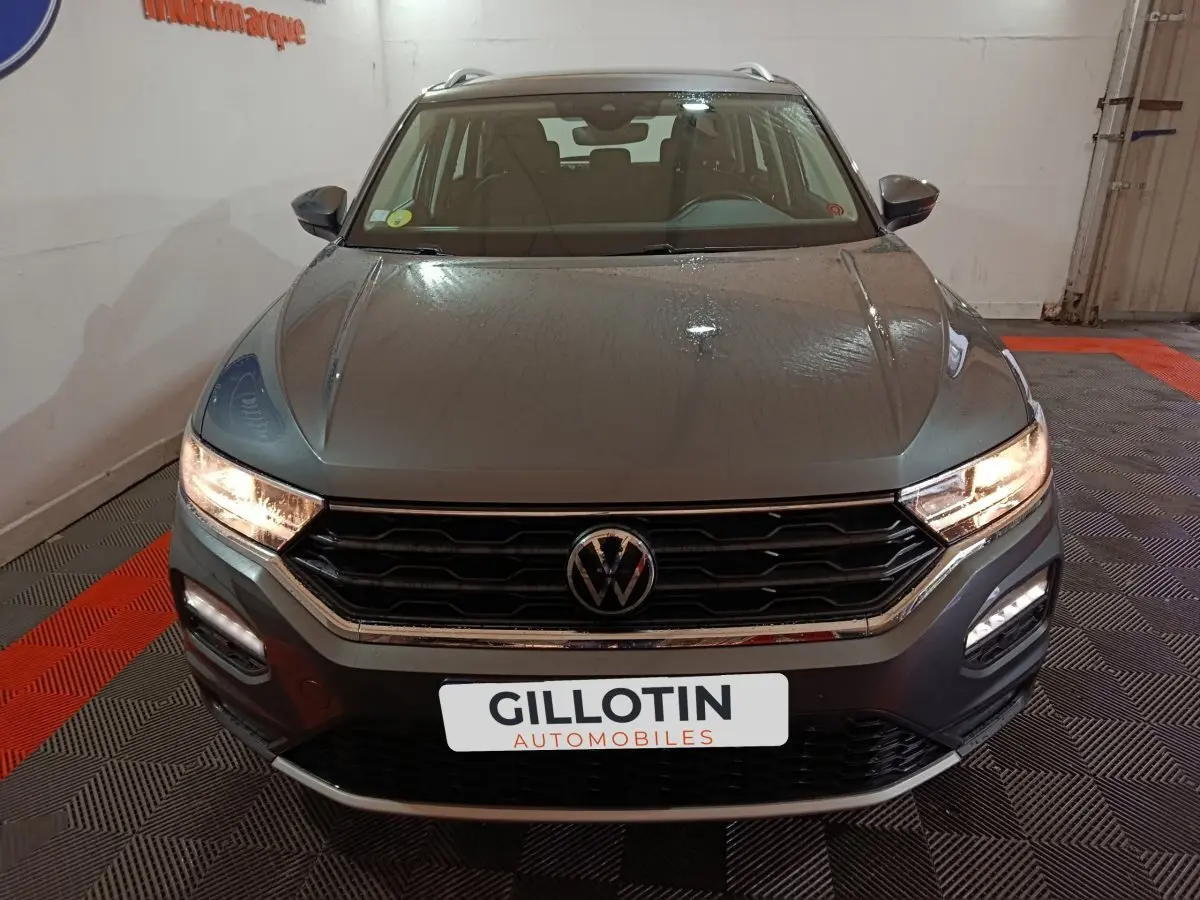 Vue frontale d’un Volkswagen T-Roc gris foncé avec feux allumés et calandre hexagonale distinctive.