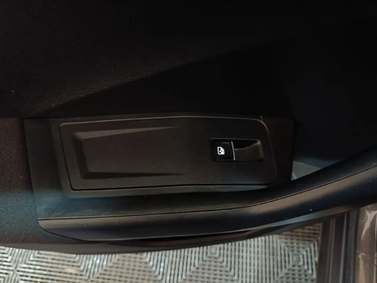 Gros plan sur le bouton d'ouverture de coffre noir, côté intérieur de porte d'un Volkswagen T-Roc gris foncé.