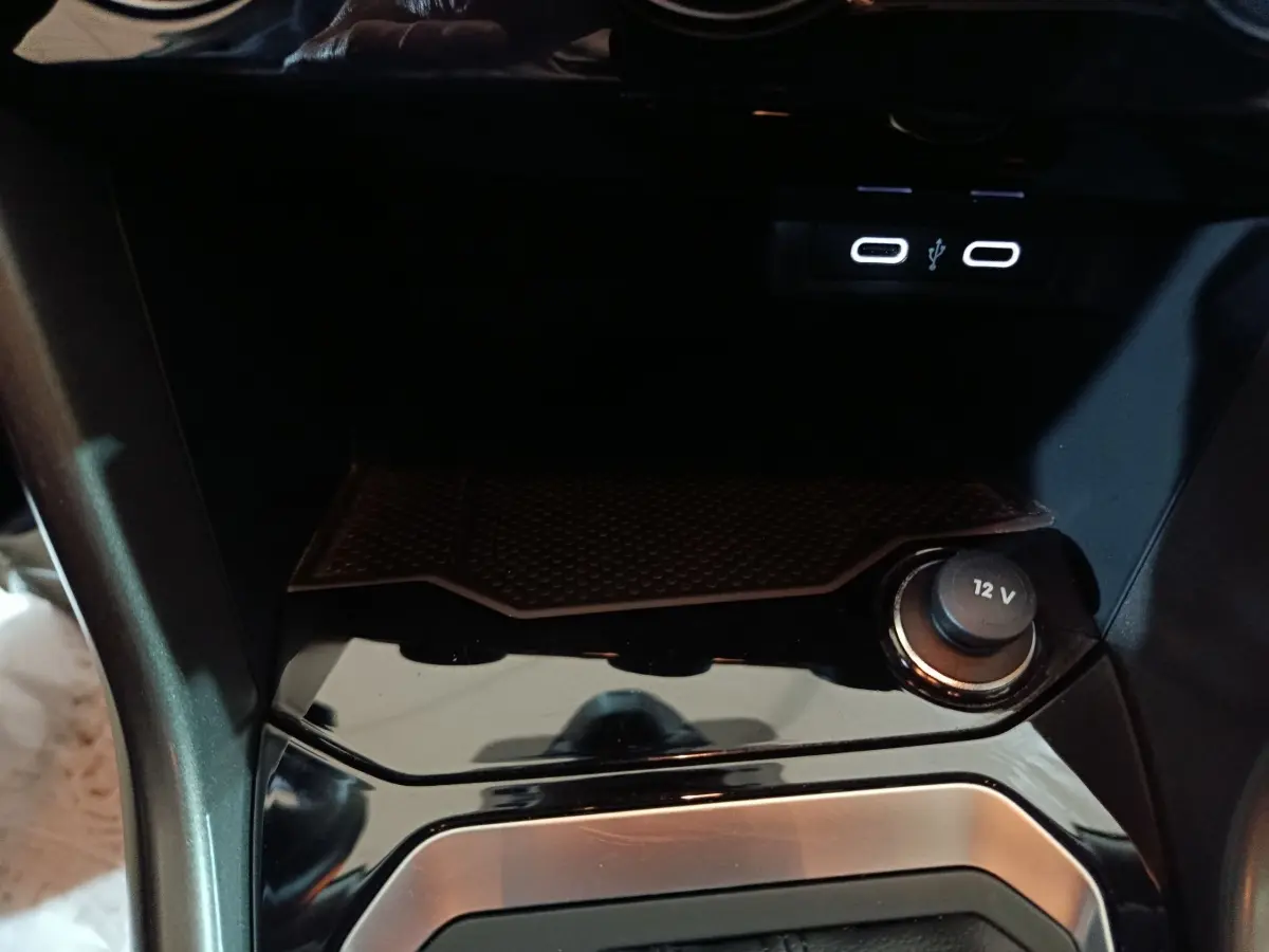 Gros plan sur la console centrale noire brillante du Volkswagen T-Roc 2.0 TDI avec prise 12V et ports USB éclairés.