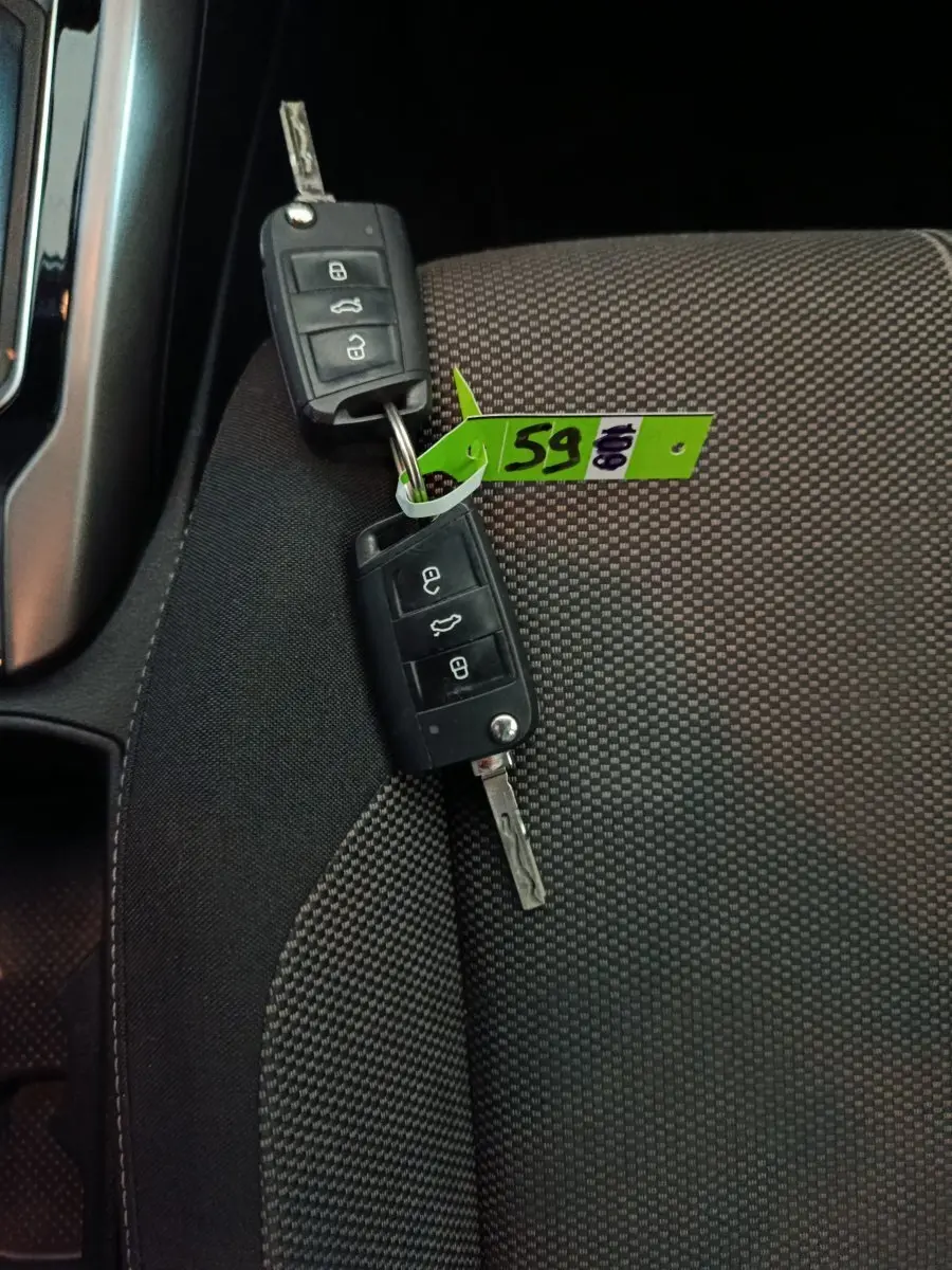 Gros plan sur deux clés Volkswagen posées sur un siège tissu gris à motifs, avec une étiquette verte attachée.