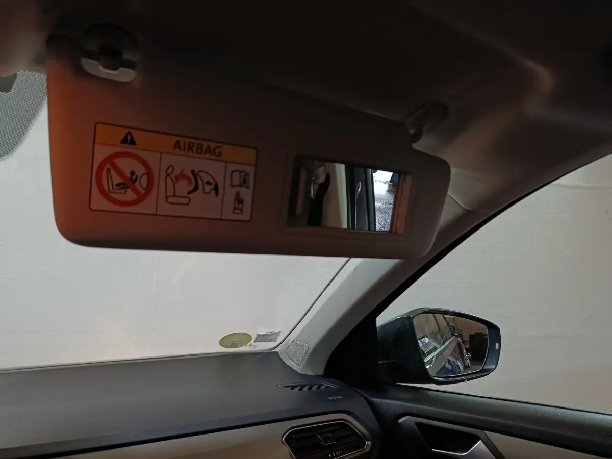 Vue intérieure côté conducteur du Volkswagen T-Roc gris foncé, montrant le pare-soleil avec miroir et rétroviseur latéral droit.