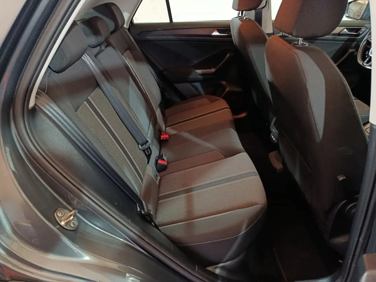 Vue intérieure côté arrière gauche du Volkswagen T-Roc gris foncé, montrant la banquette arrière en tissu avec ceintures de sécurité.