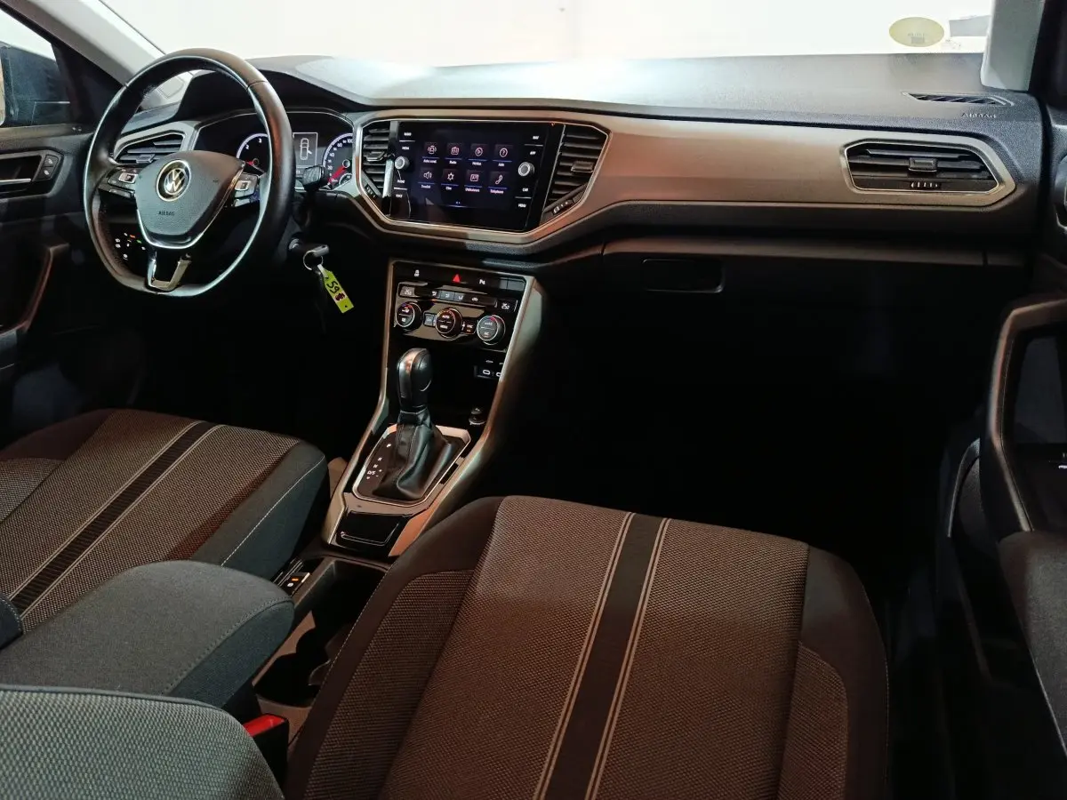 Vue intérieure côté conducteur du tableau de bord et console centrale du Volkswagen T-Roc gris foncé avec écran tactile et volant cuir.