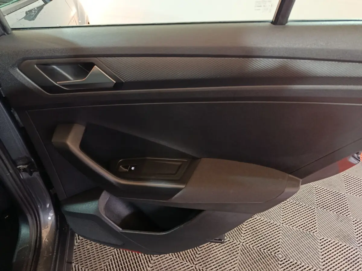 Vue intérieure de la porte côté gauche du Volkswagen T-Roc gris foncé, avec poignée et commande de lève-vitre.