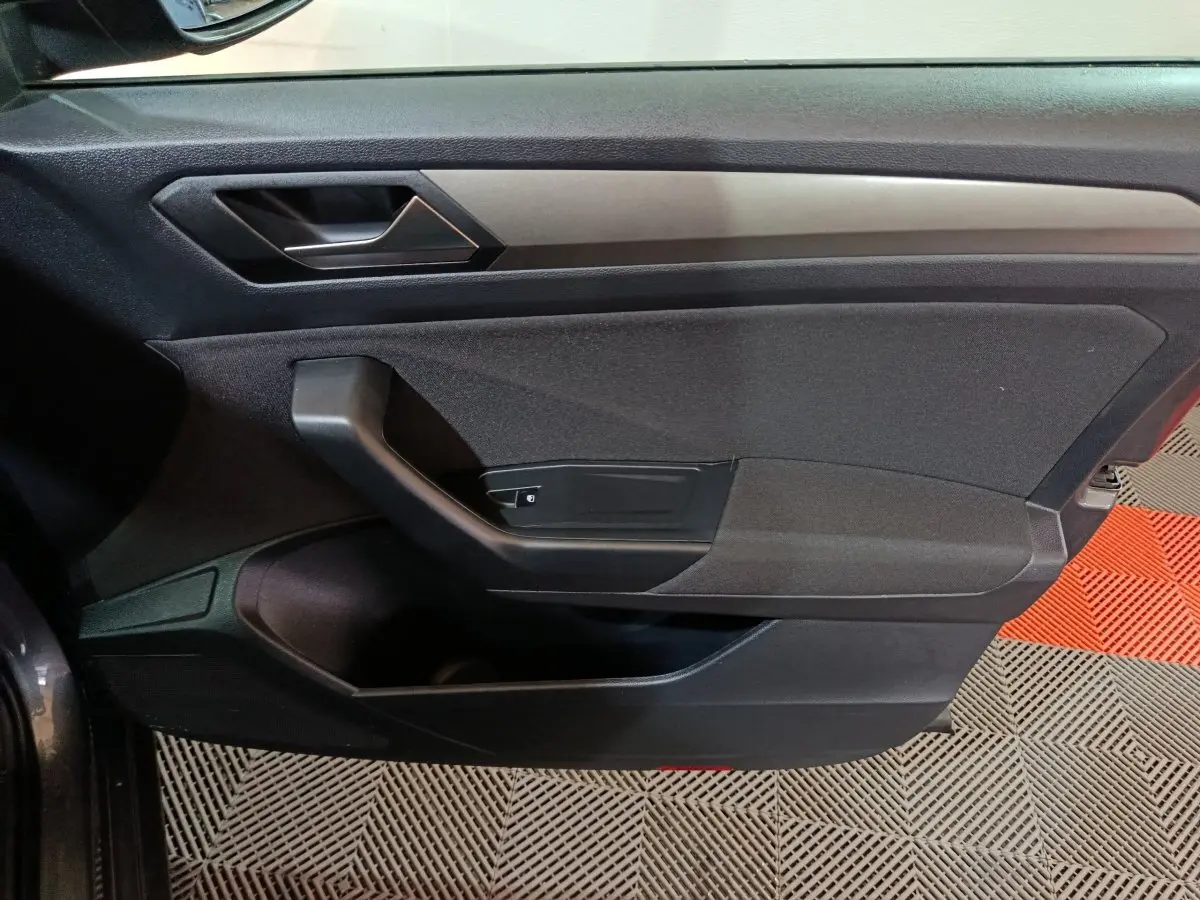 Vue rapprochée de la porte côté gauche du Volkswagen T-Roc gris foncé, montrant la poignée intérieure et les commandes.