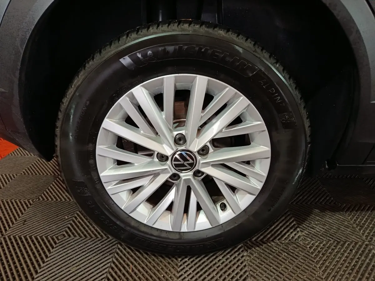 Gros plan sur la roue avant droite d’un Volkswagen T-Roc gris foncé, jante alliage argentée à multiples branches.