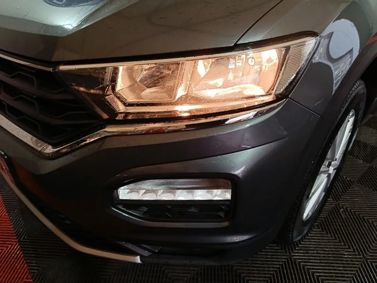 Gros plan sur l'avant droit gris foncé du Volkswagen T-Roc 2021, mettant en valeur le phare allumé et le feu antibrouillard.